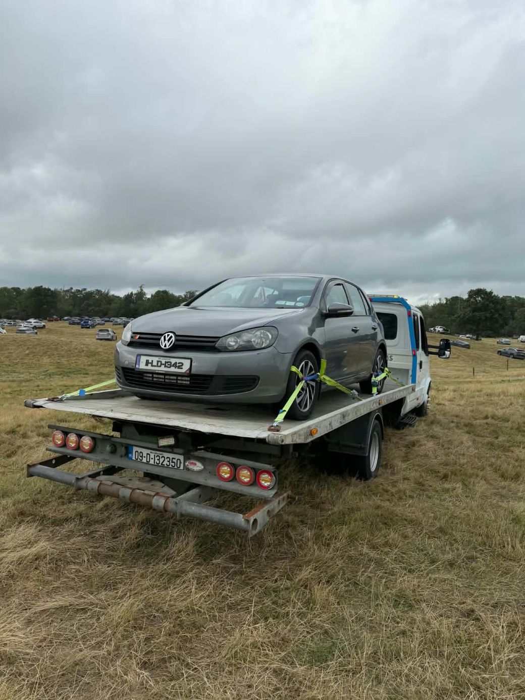 Grey Volkswagen Golf strapped to the flatbed of a recovery truck in a field