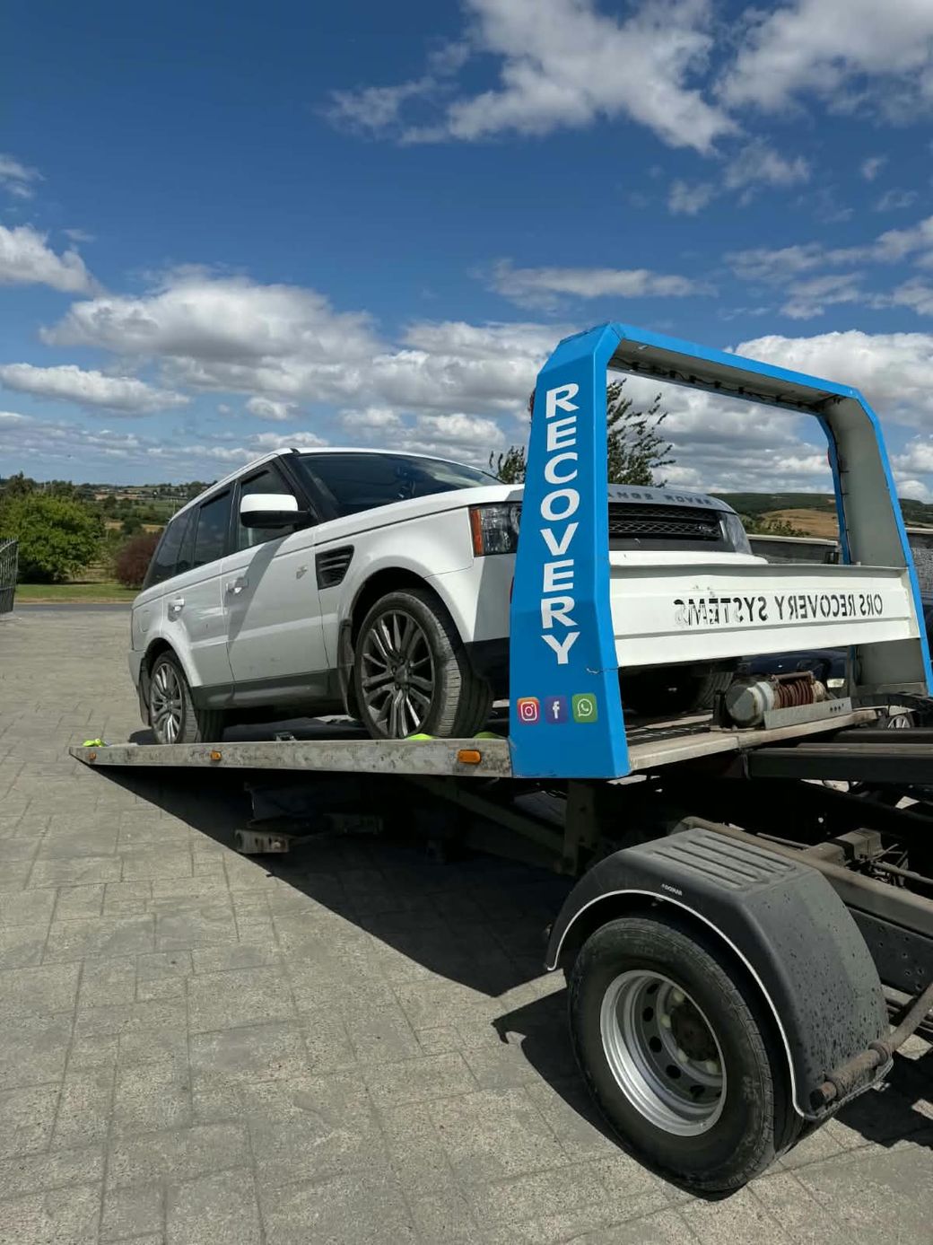 Close view of a white Range Rover Sport secured with wheel straps on a recovery truck bed
