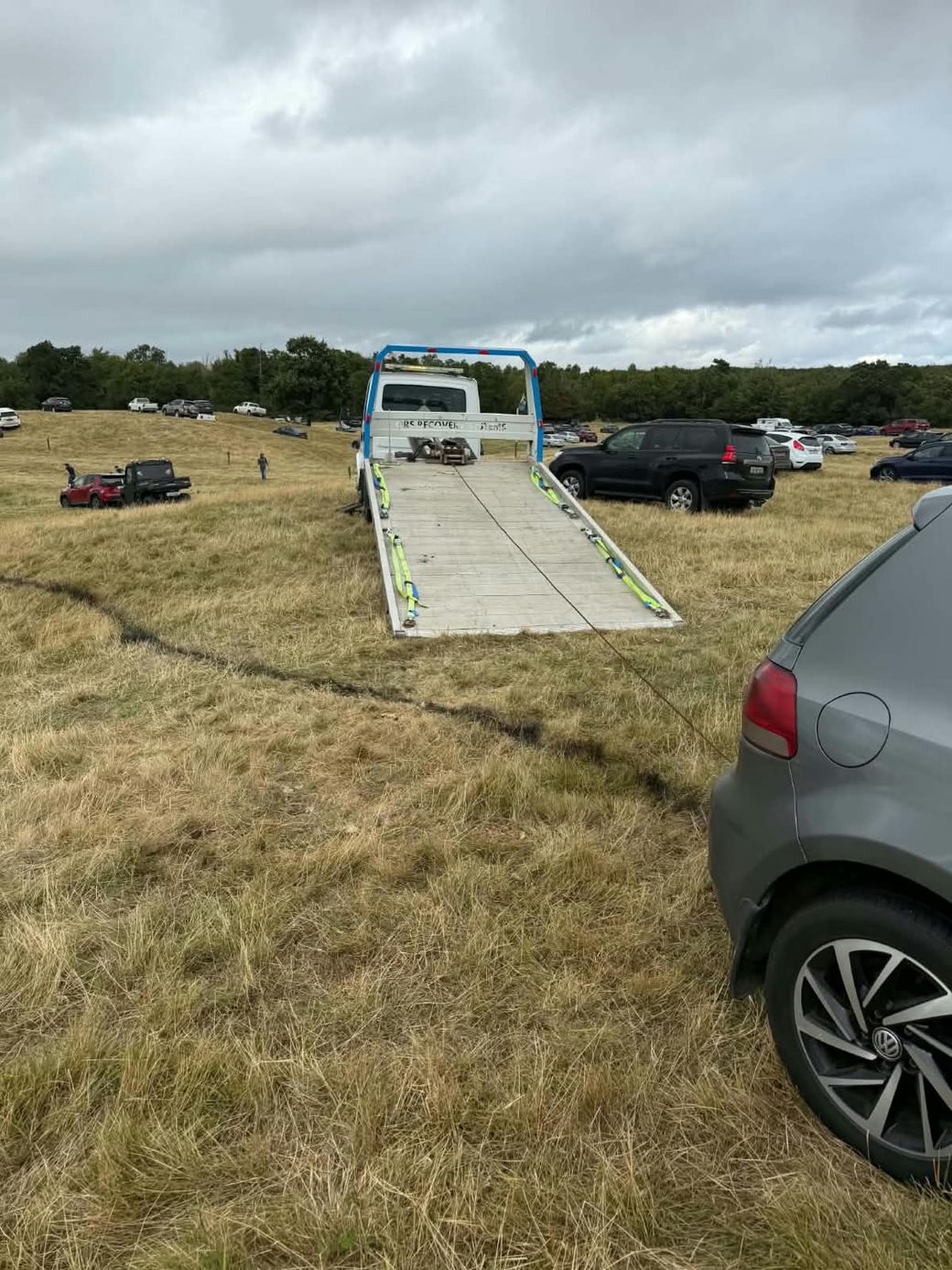 Recovery truck with tilted bed and winch cable extended, recovering a car from a grass field